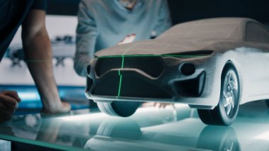 Kıdemli otomotiv mühendisleri, bir heykel prototip araba modelinin önünde mükemmellik için yeşil lazer ışığını kullanarak araba tasarımını tartışıyor. Yüksek teknoloji laboratuarında cam bir masaya yerleştirilmiş model bir araba..