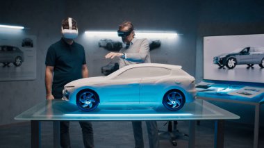 VR kulaklıklı ve joystickli otomotiv mühendisleri yüksek teknolojili bir ofiste prototip modelinin önünde dururken araç üretiminden bahsediyorlar. Araba tasarım analizi ve gelişimi.