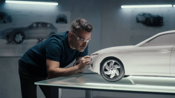 Senior automotive design engineer uses a rotary tool for perfecting the rake sculpture of a car model in a high tech company. Engineer wearing safety goggles works in an automotive company.