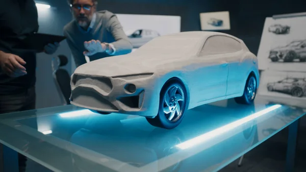 Experienced automotive designers and car developers discuss the design infront of a rake sculpt prototype car model. Engineers use a touch screen digital tablet in a high tech laboratory.
