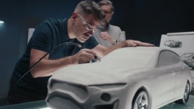 Otomotiv mühendisi, üst düzey meslektaşıyla tartışırken bir değirmen aracı kullanarak bir prototip araba modeli üzerinde çalışıyor. Yenilikçi teknolojileri olan yüksek teknoloji araba tasarım şirketi..