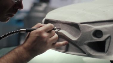 Üst düzey araba tasarımcısı ve geliştirici yüksek teknoloji bir stüdyoda bir prototip araba modelinin tırmık heykelini bilemek için kalem tipi döner bir araç kullanır. Tasarım düzeltmelerini yapıyor. Otomotiv endüstrisi.