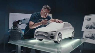 Otomotiv mühendisi bir araba prototipi heykelinin tasarım düzeltmelerini yapıyor. Değirmen makinesini kullanarak mükemmelleştiriyorum. LED 'li bir yüksek teknoloji laboratuarı ve yeni bir araba modelinin taslakları..