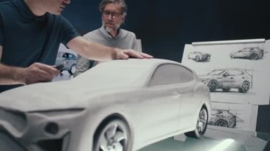 Kıdemli otomotiv mühendisleri tasarımın kalem çizimlerine bakan arabanın prototip modeli üzerinde çalışıyorlar. Masaya yerleştirilen tırmık heykelinin son rötuşları için döner bir araç kullanmak.