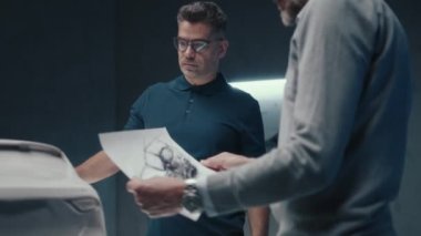 Deneyimli araba tasarımcıları ve geliştiriciler prototip araba heykelinin önünde dururken arabanın tasarımını tartışırlar. Yüksek teknoloji ürünü bir otomobil imalat şirketinin kalem çizimlerini kullanarak..
