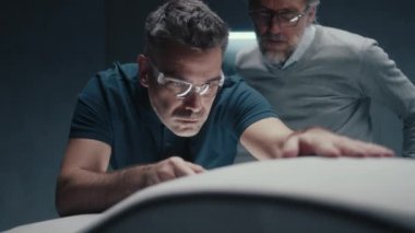 Güvenlik gözlüklü tasarım mühendisi kalem tipi bir araçla bir prototip araba modeli üzerinde çalışıyor. Bir meslektaşımla tartışırken tasarım düzeltmeleri yapıp mükemmelleştiriyorum..