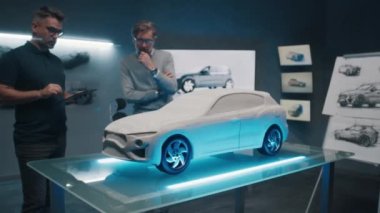 Deneyimli otomotiv tasarımcıları ve geliştiriciler yüksek teknolojili bir araba laboratuarında tırmık heykeli prototip araba modelinin önünde tasarımı tartışıyor. Dokunmatik ekran dijital kullanarak tasarım düzeltmeleri yap