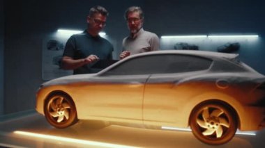 Deneyimli otomotiv mühendisleri son tasarım değişikliklerini yapmak için ışığın farklı renklerini kullanarak prototip araba modelini inceliyorlar. Bir yüksek teknoloji araba imalatında dijital dokunmatik ekran tableti kullanmak