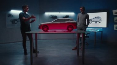 Kıdemli otomotiv mühendisleri cam bir masaya yerleştirilen prototip araba modelini ışığın farklı tonlarında ve renklerinde inceliyorlar. Bir yüksek teknoloji otomobil imalat şirketinde dijital dokunmatik ekran tableti kullanmak..