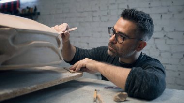 Kıdemli araba tasarımcısı, tasarımda pürüzsüz detaylar yaratmak için ahşap şekillendirme ve döngü araçları kullanan bir çevre dostu elektrikli araba prototipi üzerinde çalışıyor. El yapımı araba heykeli kilden yapılmış..