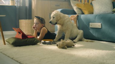 Genç kız oyuncak ve topla oynuyor, yumuşak halıda oturuyor, köpek yavrusunu besliyor, evcil hayvanla konuşuyor ve eğleniyor, evde boş zaman geçiriyor. Golden retriever.