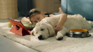 Genç kız film seyrediyor, yastığa sarılıyor, köpek uyuyor ve hafif bir halıda rüya seyrediyor, boş zamanlarını evde birlikte geçiriyorlar. Golden retriever.
