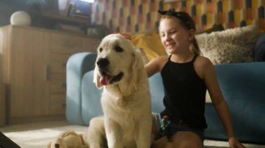 Genç kız köpekle oynuyor, gülümsüyor ve gülüyor, yumuşak halıda birlikte oturuyor, evde en iyi arkadaşıyla vakit geçiriyor. Golden retriever.