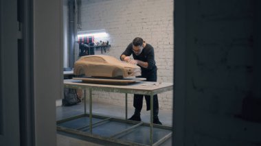 Bir atölyedeki ahşap bir masaya kilden yapılmış bir arabanın prototip modelini yapan önlük tasarımcısı. Ayrıntılı tasarım oluşturmak için yontma araçları kullanır.