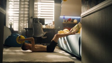 Genç çocuk koltukta elinde ve bacaklarında futbol topu tutarken karın kasları yapıyor. Futbol maçı için hazırlıklar. Futbol, spor, egzersiz, antrenman ve spor konsepti.