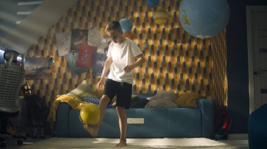 Genç hevesli çocuk, maçtan önce odasında futbol oynuyor. Okul futbol takımı oyuncusu. Renkli duvarları, çalışma masası ve sandalyesi olan modern bir oda..