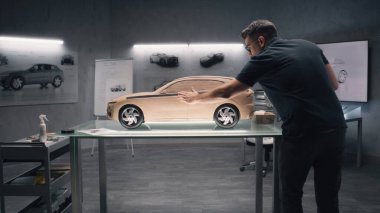Modern araba tasarım stüdyosunda iki erkek otomotiv tasarımcısı model araba üretiyor. Biri plastik killi heykel, diğeri dokunma masasında çalışıyor. Çevre dostu elektrikli arabanın gelecekteki tasarımı.