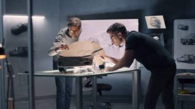 İki erkek otomotiv tasarımcısı, elektrikli arabanın fütüristik plastik kil modelini tırmık ve diğer aletlerle yontuyorlar. Modern araba tasarım stüdyosunda çalışıyorum..