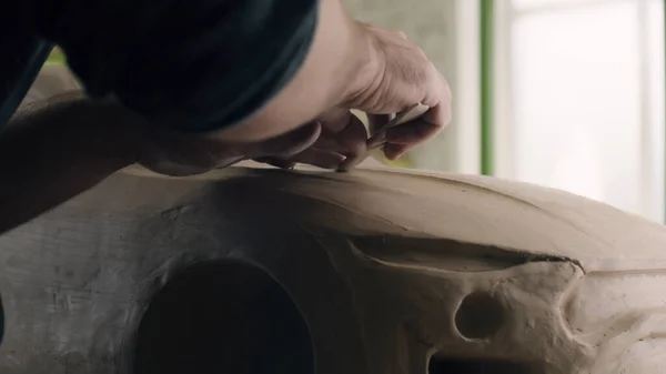 Closeup hands of a car designer works on the design details of an unfinished sculpture of the prototype eco-friendly electric car model. Hand made car sculpture on a wooden table.