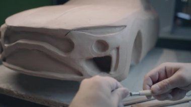 Deneyimli araba tasarımcısı, arabanın prototip çevre dostu elektrikli modeli üzerinde çalışıyor. Tasarımda detaylar için kilden parçalar oymak için yontma aracı kullanıyor. El yapımı araba heykeli kilden yapılmış..