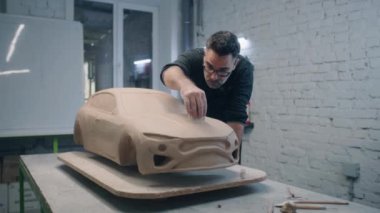 Kıdemli otomotiv tasarımcısı, kilden yapılmış arabanın prototip modelini heykel aletleriyle yontuyor. Deneyimli tasarımcı bir atölyede çalışıyor. Otomotiv endüstrisi.