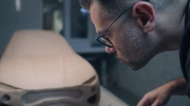Deneyimli araba tasarımcısı, tasarımda pürüzsüz detaylar yaratmak için ahşap şekillendirme araçları kullanan çevre dostu elektrikli arabanın prototip modeli üzerinde çalışıyor. El yapımı araba heykeli kilden yapılmış..