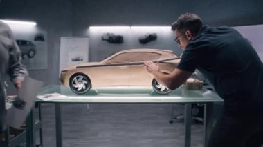 Modern araba tasarım stüdyosunda iki erkek otomotiv tasarımcısı model araba üretiyor. Biri plastik killi heykel, diğeri dokunma masasında çalışıyor. Çevre dostu elektrikli arabanın gelecekteki tasarımı.
