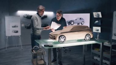 İki erkek otomotiv tasarımcısı modern araba tasarım stüdyosunda elektrikli arabanın çevre dostu modeli üzerinde çalışıyor. Biri plastik killi heykel, diğeri 3 boyutlu bilgisayar yazılımında çalışıyor..