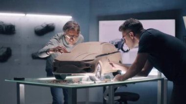 İki erkek otomotiv tasarımcısı, tırmık ve diğer aletlerle fütürist plastik kil çevre dostu elektrikli araba üretiyor. Modern araba tasarım atölyesinde çalışıyorum. Yeni nesil araba modeli şekillendiriliyor.