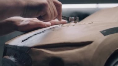 Erkek otomotiv tasarımcısının plasticine kil ve tırmıkla fütüristik araba modeli üzerinde çalışırken yakın plan çekimi. Yeni nesil elektrikli arabanın gelecekteki tasarımı. Modern araba tasarım stüdyosunda çalışıyorum..