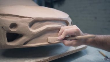 Erkek bir tasarımcının elleri heykel aletleri kullanarak bir araba heykeli üzerinde çalışır. Bitmemiş modelin yüzeyini bir atölyede pürüzsüzleştirir. Otomotiv endüstrisi.