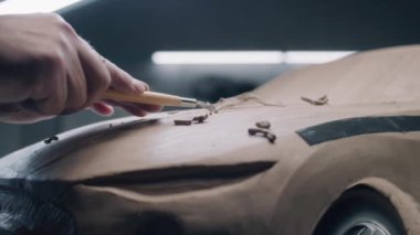 Erkek otomotiv tasarımcısının plastik kil ve tırmıkla çevre dostu elektrikli araba modelini şekillendirdiği yakın çekim. Yeni nesil elektrikli arabanın gelecekteki tasarımı. Modern araba tasarım stüdyosunda çalışıyorum..