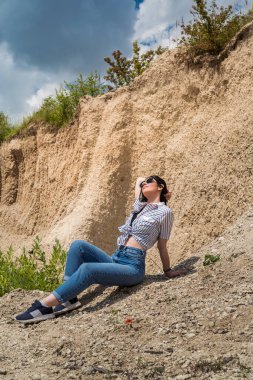 Gündelik giysiler içinde genç ve güzel bir bayan kum ocağında dinleniyor, tatilde ve yaz tatilinde seyahat ediyor.