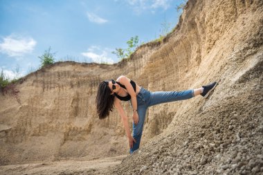 Taş ocağındaki kum kayalarının üzerinde poz veren sıradan giysili sıska bir kız. yaz zamanı