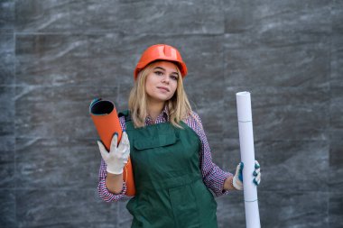 Kırmızı üniformalı, miğferli, koruyucu eldivenli kadın kameraya poz veriyor ve daireyi onarmaya hazırlanıyor. İnşaat işgali. 