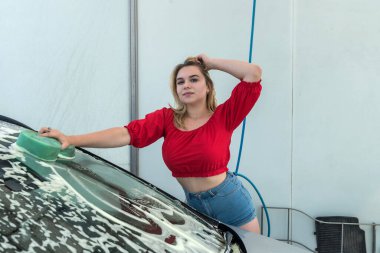 El yıkama servisindeki güzel kadın sürücü. Oto pisliğini temizlemek için sünger beyaz köpük kullan.