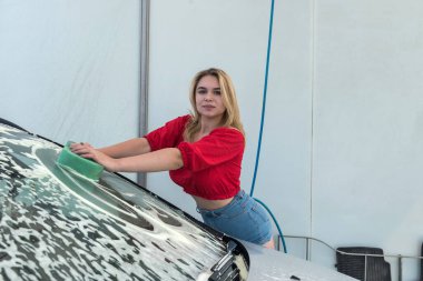 Güzel bayan sürücü köpüğü yeşil süngerle yıkıyor. Arabasını pislikten temizliyor.
