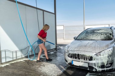 Güzel spor kadın araba yıkamada köpükle araba yıkar.