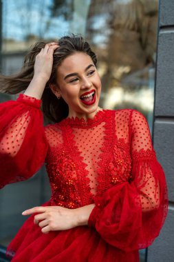 Güzel, şık, esmer kadın şehir arka planında kırmızı elbiseli poz veriyor.