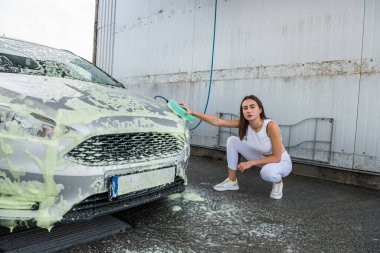 El yıkama servisindeki güzel kadın sürücü. Oto pisliğini temizlemek için sünger beyaz köpük kullan.