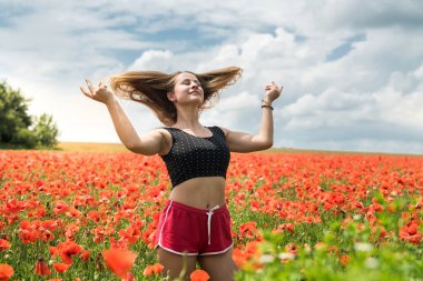 Siyahlar içinde genç, sıska bir kadın çiçek açan gelinciklerle sahada, doğada özgürlük.