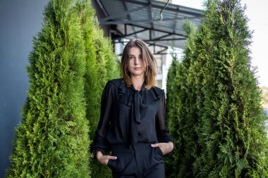 Doğada siyah elbiseli çekici genç bir kadın, arka planda beyaz sedir.