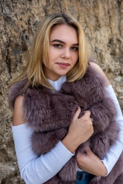 Yaz mevsiminde kum kayalarının yanında poz veren kürklü ve günlük giysili genç bayan portresi.