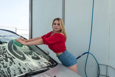 Güzel kadın sürücü ön camı süngerle yıkıyor. Manuel istasyonunda kirli arabasında süngerle.