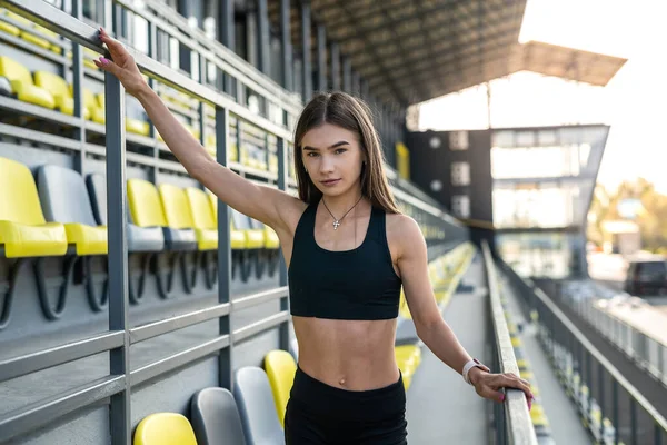 pretty slim woman in sport wear resting after hard workout near chairs on modern stadium. enjoy summer day