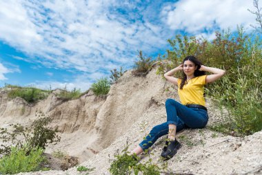 Taş ocağında ya da kanyonda, kayanın yanındaki kumların üzerinde duran sıska genç bir kadın. Mükemmel yolculuğun için yaz zamanı.