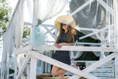 Genç bayan yazın beyaz çardakta gölün yanında poz veriyor.