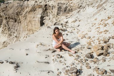 Açık beyaz elbiseli güzel, şehvetli genç bir kadın yaz zamanı beyaz kumların üzerinde uzanıyor.