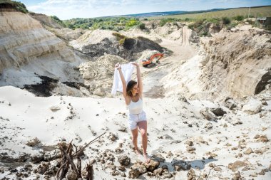 İnanılmaz çekici beyaz elbiseli genç kız boş zamanlarında kumlu bir kanyon ocağında dinleniyor.
