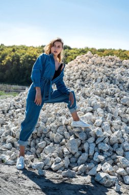 Mavi tulumlu güzel bir kadın büyük beyaz kök taşları arasında poz veriyor. Kariyer. Yaşam biçimi